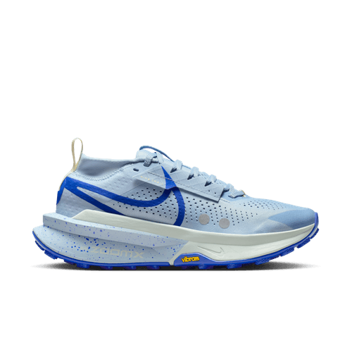 Nike Zegama 2 Dame i LT Armory Blue/Racer Blue vises i sideprofil med en lyseblå overdel, tyk spættet sål, blå swoosh og accenter, hvide snørebånd og et gult Vibram-logo på mellemsålen mod en almindelig hvid baggrund.