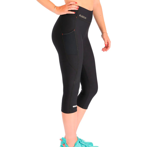 Den nederste halvdel af en person ses i profil iført Fusion 3/4 Training Tights, Dame, SuperBlack med sidelommer og en tætsiddende Fusion-linning, sammen med turkise løbesko.