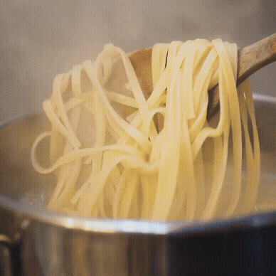 En træske løfter kogte fettuccine-nudler op af en dampende gryde med kogende vand.