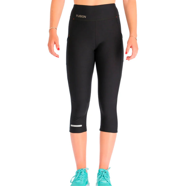 En person iført Fusion 3/4 Training Tights, Dame, SuperBlack med et FUSION-logo på den høje linning, turkise løbesko, på en hvid baggrund. Personens hoved er ikke synligt.