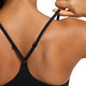 Nærbillede af en kvindes ryg iført Nike Padded Adjustable Sports Bra, Dame, Black/Black. Hun justerer den højre strop. Den ensfarvede hvide baggrund fremhæver det slanke design og Dri-FIT-teknologien.