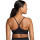 En kvinde med mørkt hår i en hestehale ses bagfra iført Nike Padded Adjustable Sports Bra, Dame, Black/Black. Sports-bh'en har tynde stropper og Nike-logoet på elastikken mod en hvid baggrund.