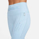 Nærbillede af en person iført Nike Trail High-Waisted 7/8 Leggings til kvinder i Lt Armory Blue/Lt Orewoord Brn/Khaki, med bælte, lynlåslomme, karabinhage og "Nike Trail"-tekst på låret mod en hvid baggrund.