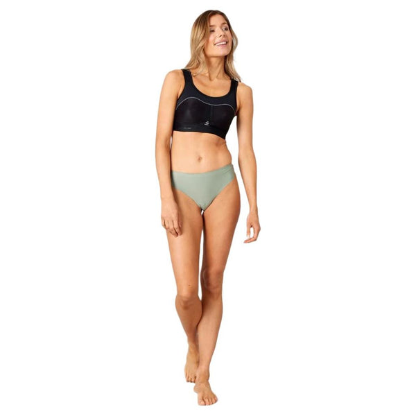 En kvinde står barfodet på en hvid baggrund, smiler og kigger til siden. Hun er iført Purelime Compression Bra High Impact, Dame, i sort, sammen med lysegrønt undertøj, med den ene hånd afslappet ved siden af sig.