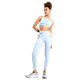 En kvinde poserer i Nike Trail High-Waisted 7/8 Leggings (Dame, Lt Armory Blue/Lt Orewoord Brn/Khaki) med en lyseblå Dri-FIT sports-bh og hvide sneakers. Hendes krøllede hår er sat op, og hun bærer en lille pose på linningen mod en hvid baggrund.