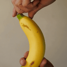 En hånd skræller en moden gul banan på en almindelig, lys baggrund.