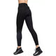 En person ses fra taljen og ned iført Nike Trail High-Waisted 7/8 Leggings til kvinder i Black/Dk Smoke Grey/Dk Smoke Grey og sorte sportssko med hvide såler, stående mod en almindelig hvid baggrund.