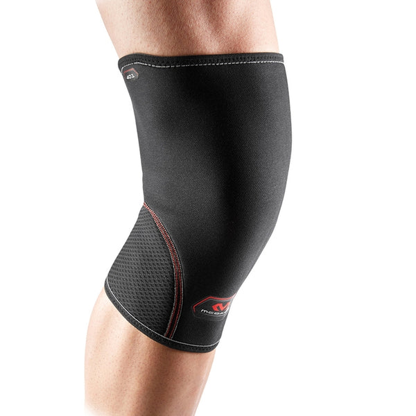Et nærbillede viser en persons ben iført McDavid Knee Support Sleeve Neoprene, Unisex, Black, med røde syninger og et lille logo på en almindelig hvid baggrund.