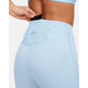 En person i Nike Trail High-Waisted 7/8 Leggings (Lt Armory Blue/Lt Orewoord Brn/Khaki) putter en sort smartphone i baglommen på linningen, mens hun har en matchende lyseblå top på.