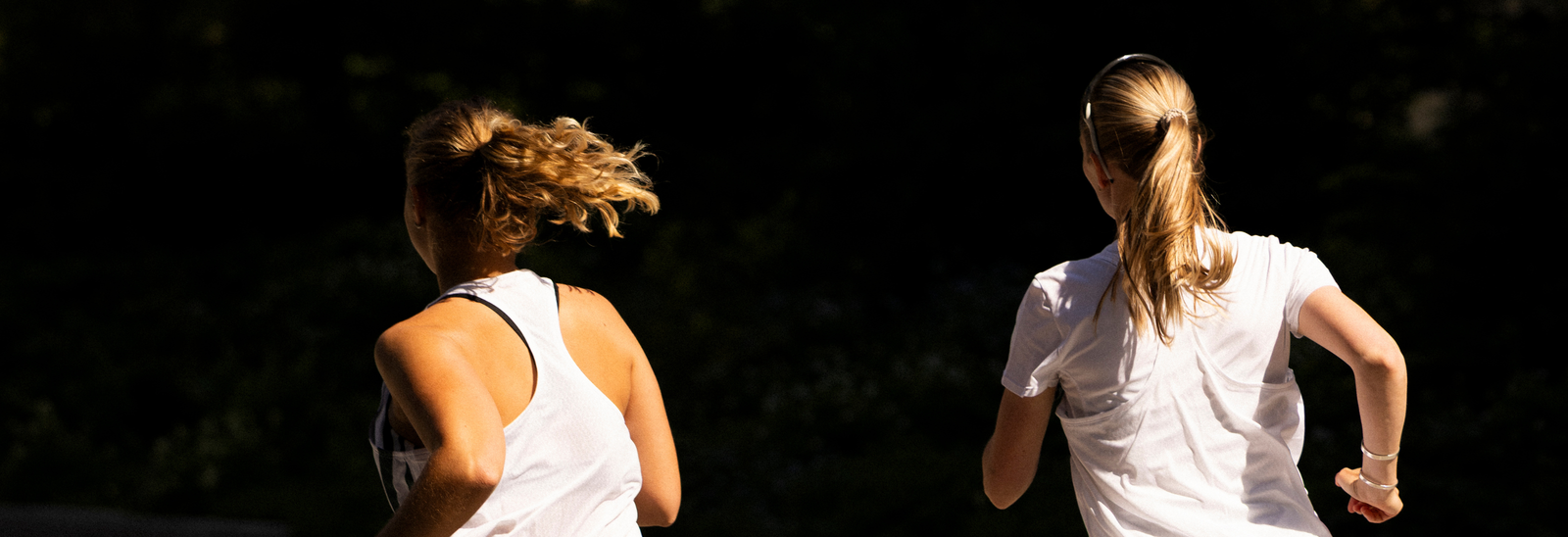 En kvinde i sportstøj løber langs en sti ved siden af et vandløb med synlige bygninger i baggrunden og sollys, der oplyser scenen.