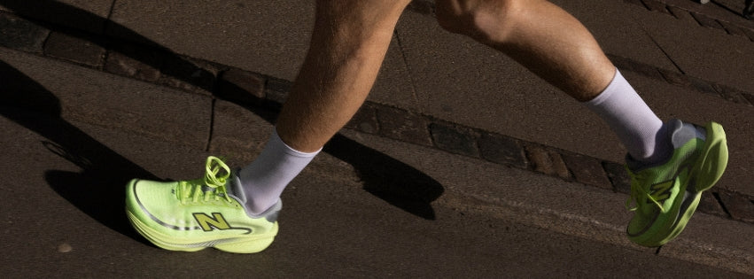 To sportssko, en beige med brune detaljer og en gul med hvide og grå detaljer, er arrangeret mod en beige baggrund med gradient.