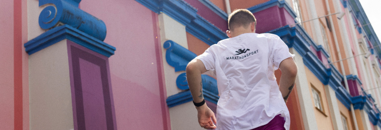 En person iført en lysegrøn langærmet skjorte, matchende hue og mørke solbriller står udendørs og justerer huen med begge hænder. Skjorten og huen har begge et Adidas-logo.