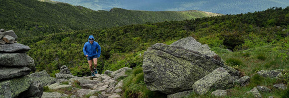 En person iført en grøn skjorte og en sort Patagonia-rygsæk ses bagfra. Personen har også et smartwatch på sit venstre håndled. Baggrunden er et abstrakt vægmaleri.