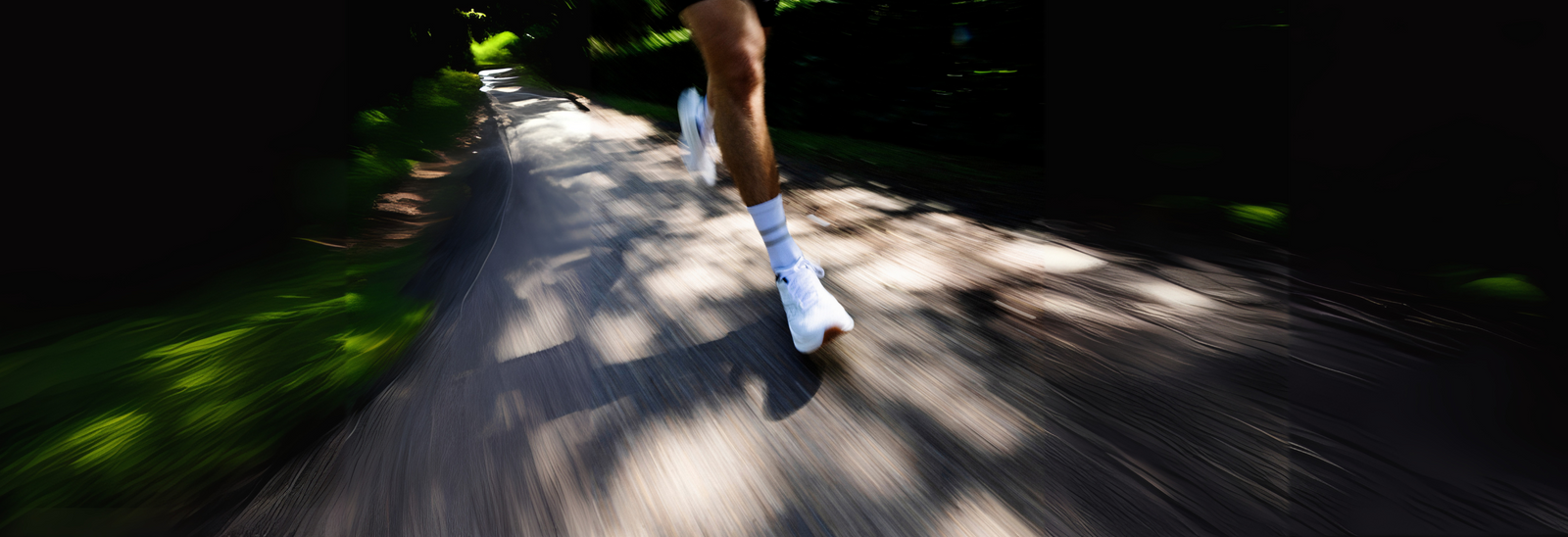 En person løber på en sti omgivet af grønt, med benene og de hvide løbesko i fokus og en gruppe mennesker sløret i baggrunden.
