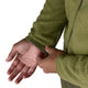 En person iført Patagonia R1 Air Jacket, Herre, Caper Green justerer ærmet med den ene hånd. Den monterede manchet og den synlige søm er vist, og billedet er beskåret, så man kun ser overkroppen og hænderne.