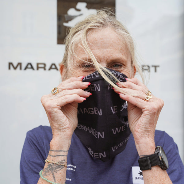 En ældre person med lys hud og lyst hår bærer Marathon Sport Multiscarf, Unisex, Sort fra Marathon Sport – trukket op over næsen, så de markante blå øjne kommer til syne. Iført en blå skjorte med ur, ringe og en synlig tatovering på armen demonstrerer vedkommende med selvtillid, hvordan dette halsedisse til udendørs brug er ideelt som stilfuldt løbetilbehør.