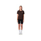 En person står på en hvid baggrund iført en Liiteguard Ground-Tech T-shirt, Dame, Coffee Bean, sammen med sorte shorts, hvide strømper og hvide sneakers. De ser fremad med armene ned langs siden.