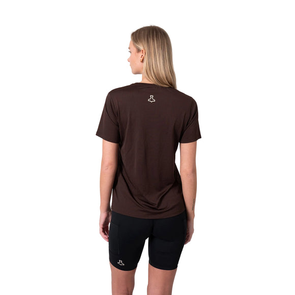 En kvinde med langt lyst hår, set bagfra mod en hvid baggrund, er iført en Liiteguard Ground-Tech T-shirt i Coffee Bean og sorte shorts. Begge dele har et lille hvidt logo på ryggen.
