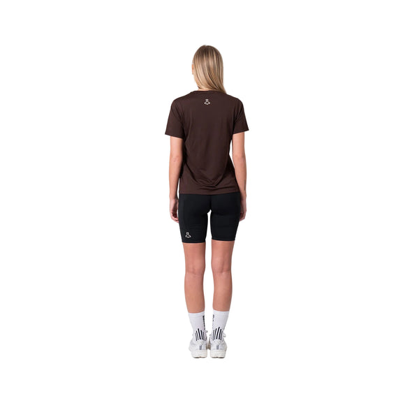 En person ses bagfra iført Liiteguard Ground-Tech T-shirt, Dame, Coffee Bean - fremstillet af S.Café-materiale - sammen med sorte shorts, hvide sokker med sorte striber og hvide sneakers på en almindelig hvid baggrund.