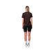 En person ses bagfra iført Liiteguard Ground-Tech T-shirt, Dame, Coffee Bean - fremstillet af S.Café-materiale - sammen med sorte shorts, hvide sokker med sorte striber og hvide sneakers på en almindelig hvid baggrund.