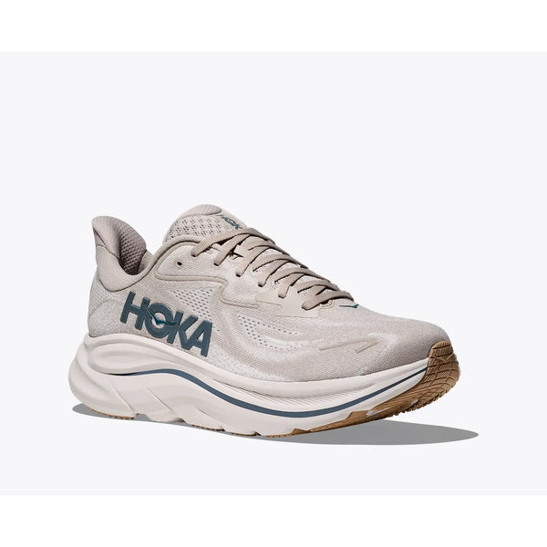 Hoka Clifton 10 Herre i Putty/Grout er en lys beige sportssneaker med en tyk polstret sål og et kraftigt blåt HOKA-mærke på siden, der vises på en almindelig hvid baggrund.