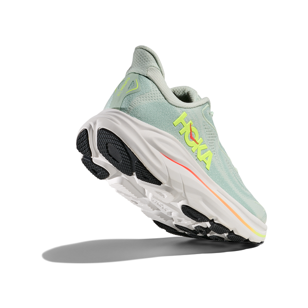 A Hoka Clifton 10 Dame løbesko i Sea Glass/Neon Flame vises fra en lav bagvinkel med tyk hvid sål, sorte og orange detaljer samt gult Hoka-logo på siden. Skoen er isoleret på hvid baggrund.