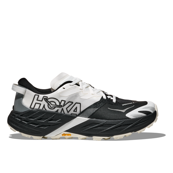 Hoka Speedgoat 7 til mænd i sort/hvid har en chunky sål, hvide snørebånd, HOKA-branding og et gult Vibram-logo på ydersålen, vist i profil på en hvid baggrund.