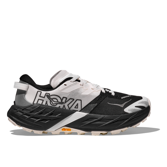 Hoka Speedgoat 7 Dame i sort/hvid har en overdel i mesh, snørelukning og Hoka-logo på siden. Den tykke sål med Vibram Megagrip sikrer et godt greb og har et orange Vibram-logo nær hælen.