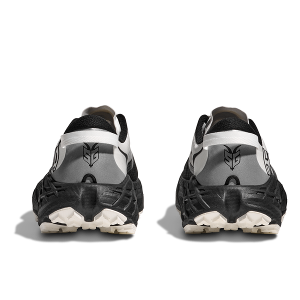 Et par Hoka Speedgoat 7 Dame i sort/hvid vises bagfra og fremhæver et stiliseret hæl-logo, sorte detaljer i bunden og strukturerede såler med Vibram Megagrip til teknisk trail-performance.