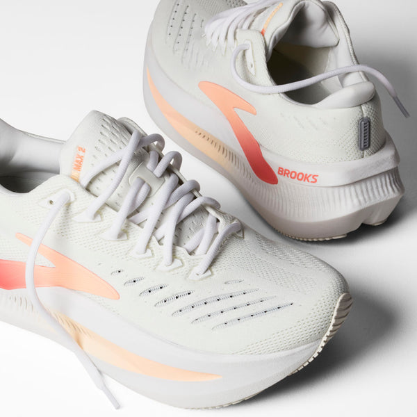 Et par Brooks Glycerin Max 2 dame løbesko i White/Coral/Peach, med tykke polstrede såler for maksimal komfort og hvide snørebånd, vises på en hvid overflade.