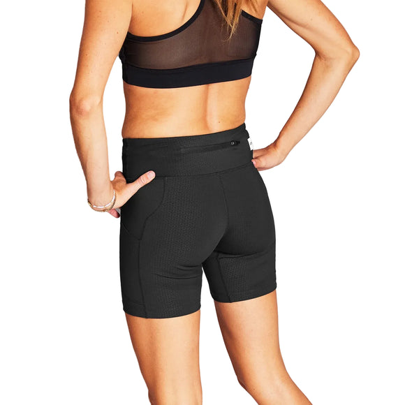 En kvinde kigger væk fra kameraet iført sorte Combat+ Short Tights 7" fra Saysky og en matchende sports-bh. Hendes højre hånd hviler på hoften, mens hendes venstre arm hænger ved siden af hende. Strømpebukserne er lavet af genbrugspolyester.