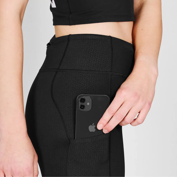 En person, der er synlig fra overkrop til hånd, iført sorte løbetights kvinder og crop top, lægger en sort smartphone i sidelommen på sine Saysky Combat+ Short Tights 7", Dame, Black - fremstillet af genanvendt polyester.
