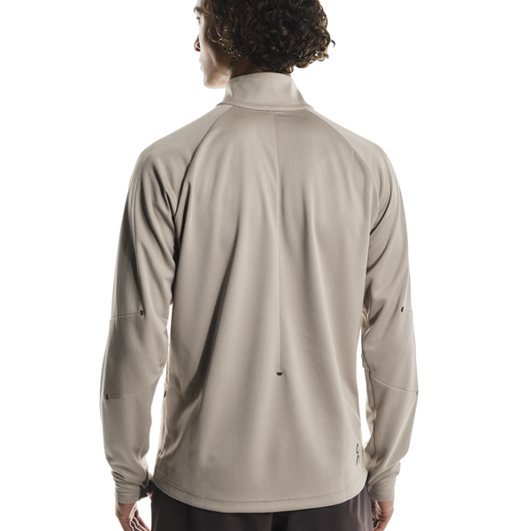 En person ses bagfra iført den løstsiddende On Climate Shirt, Herre in Desert, med høj krave, stående på en almindelig hvid baggrund.