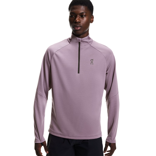 En mand står og kigger fremad iført On Climate Shirt, Herre, Dewberry - en lyslilla, svedtransporterende træningstrøje med en halv lynlås og et lille logo på venstre bryst - sammen med sorte bukser på en almindelig hvid baggrund.