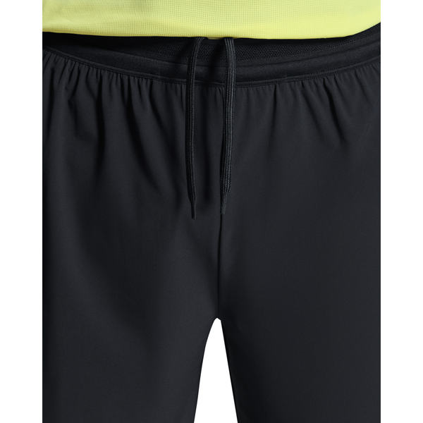 Nærbillede af en person iført On 5" Performance 2/1 Shorts, Herre, Black, lavet af åndbart materiale med løst bundne snore foran; vist fra taljen til midt på låret og sat sammen med en gul skjorte.