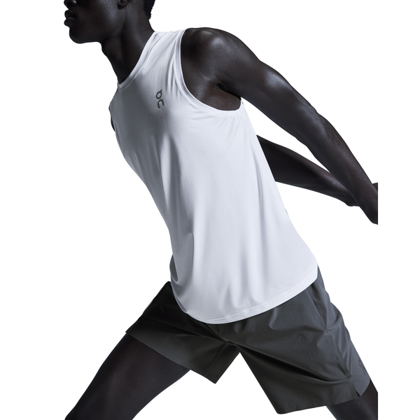 En mand i hvid ærmeløs sportstrøje og On 7" Performance Shorts, Herre, Eclipse strækker armene bagud med kroppen vinklet til siden mod en almindelig hvid baggrund.