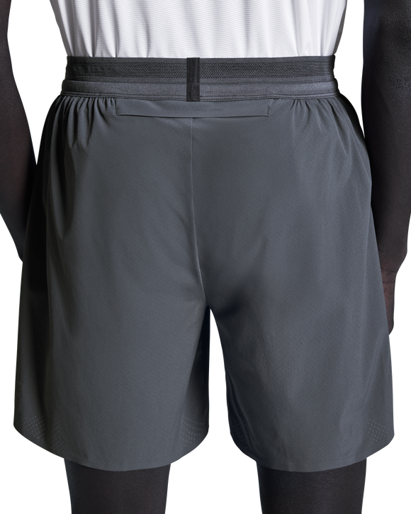 En person ses bagfra, fra taljen og ned, iført On 7" Performance Shorts, Herre, Eclipse over sorte leggings med en hvid skjorte stoppet ind.