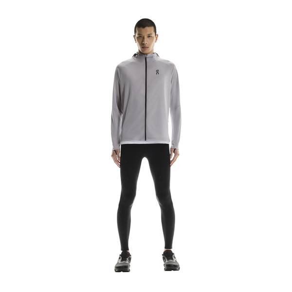 En person kigger fremad mod en hvid baggrund iført On Performance Tights, Herre, Black, sammen med en lysegrå jakke med hætte, sorte sportssko og en hvid skjorte indenunder.