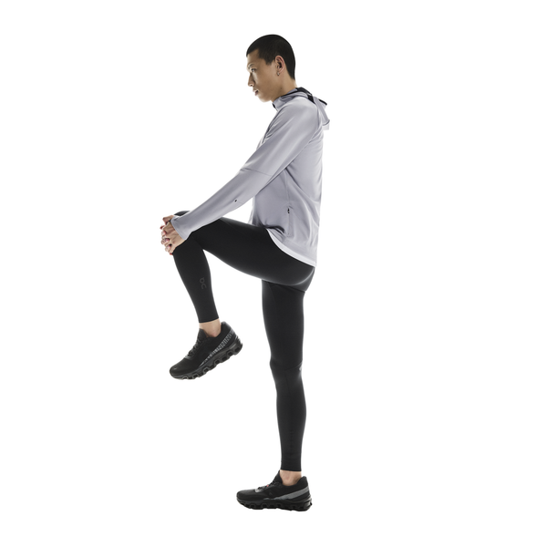En person i sportstøj står på et ben og strækker sig mod en hvid baggrund iført On Performance Tights, Herre, Black, designet til optimal præstation.