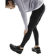 En person bærer en lysegrå langærmet top, On Performance Tights, Herre, Black, og sorte sportssko, mens han bøjer sig forover for at strække sig og røre ved sin venstre ankel på en hvid baggrund.