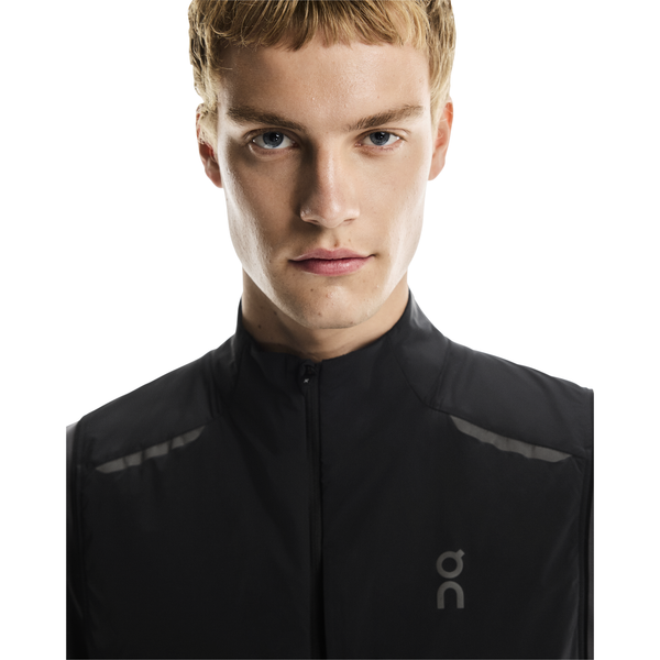 En ung mand med kort blondt hår og blå øjne bærer On Weather Vest, Herre, Black/Eclipse med et lille On-logo på brystet og ser direkte ind i kameraet mod en almindelig hvid baggrund.
