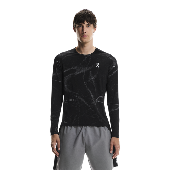 En person kigger fremad og er iført On's Performance Long-T Lumos, Herre, Black med hvidt brystlogo og lysegrå sportsshorts. Baggrunden er almindelig hvid.