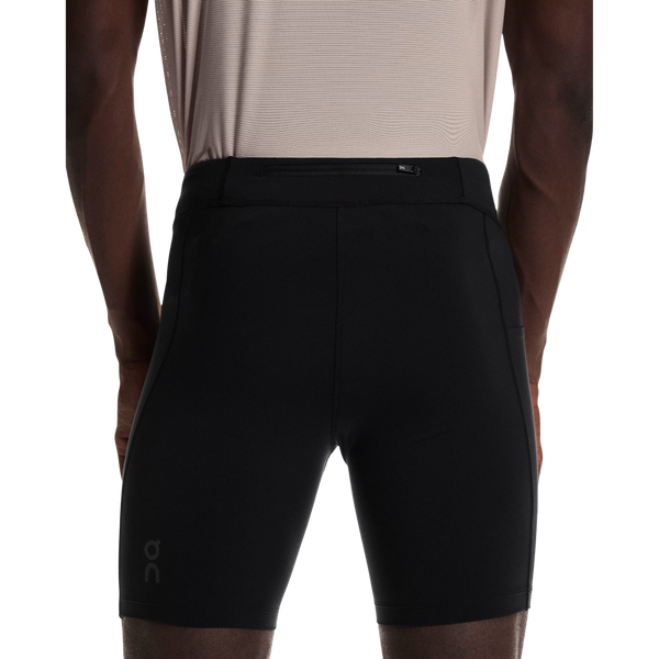 En person ses bagfra i en lys beige skjorte og On 8 Performance Tights, Herre, Black, med svedtransporterende materiale og et lille logo på venstre ben, på en almindelig hvid baggrund.