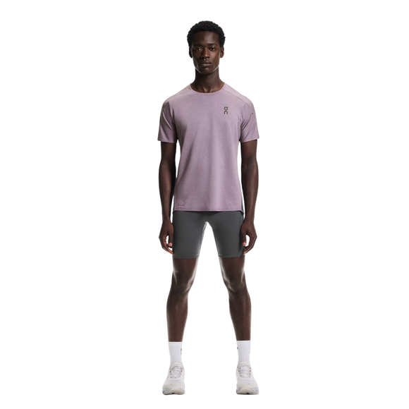 En mand står med ansigtet fremad iført en lyslilla kortærmet sportstrøje og On 8" Performance Tights, Herre, Eclipse i grå, sammen med hvide sokker og sportssko på en almindelig hvid baggrund.
