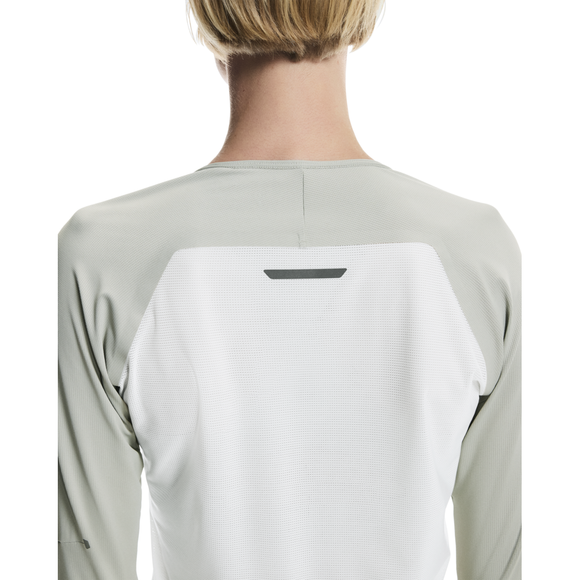 En person med kort blondt hår ses bagfra iført On Performance Long-T til kvinder i Tin/Iceberg med lysegrå og hvide farver og en lille sort refleksdetalje øverst på ryggen.