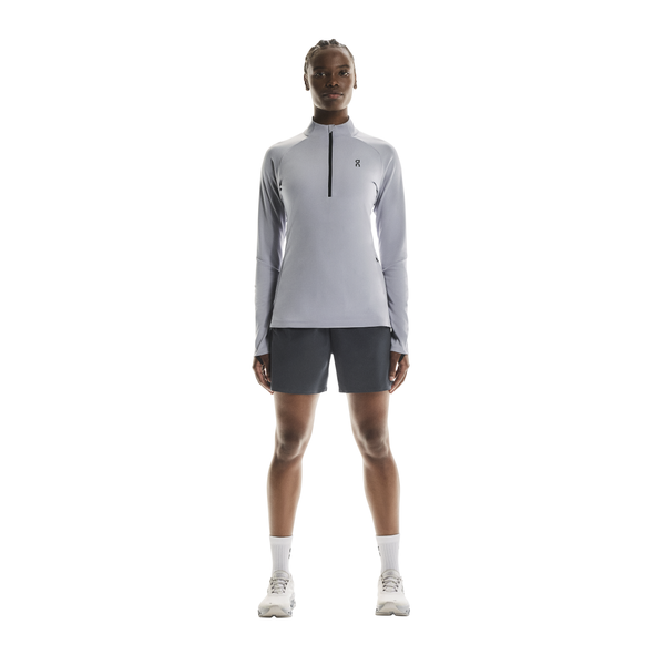 En person ser frem for sig iført en On Climate Shirt, Dame, i lilla, sammen med mørke shorts, hvide sokker og hvide sportssko mod en almindelig hvid baggrund.