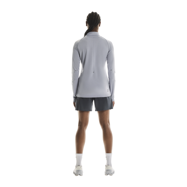 En person står med ansigtet vendt mod kameraet iført en On Climate Shirt, Dame, Lilac, mørkegrå shorts, hvide strømper og hvide sportssko på en almindelig hvid baggrund.