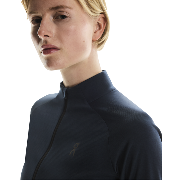 En person med kort blondt hår bærer On Climate Shirt, Dame, Navy, med høj krave og kigger lidt til siden mod en almindelig hvid baggrund.