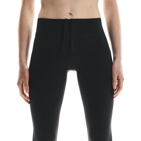 En person bærer On Performance Tights Winter, Dame, i sort med snøre i taljen, vist fra taljen til midt på låret mod en almindelig hvid baggrund.