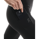 En kvinde i sorte On Performance Tights Winter, Dame, lægger en sort smartphone i sidelommen. Strømpebukserne har et lille On-logo nær lommen og er ideelle til vinterbrug.